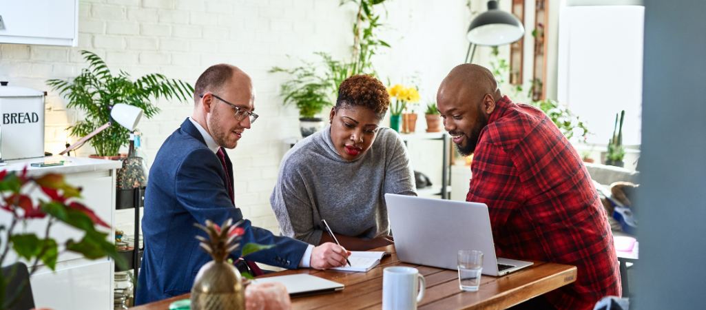 two men and one woman sitting together taking notes and reviewing computer